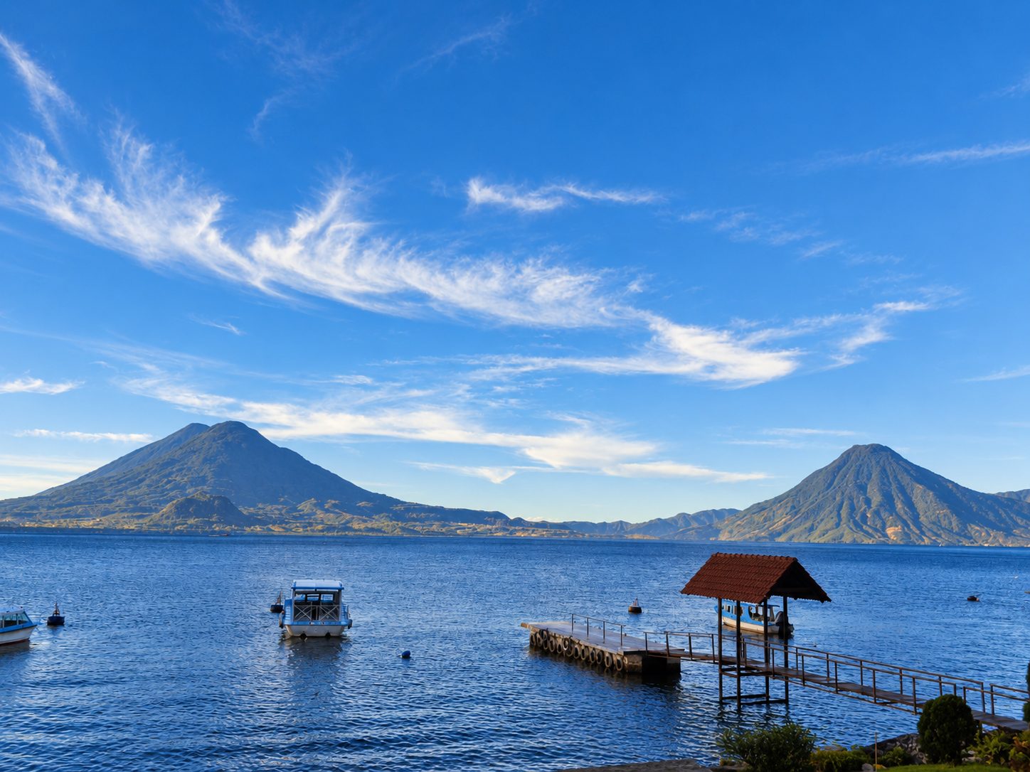 Lake Atitlán with boats, a dock, and two volcanoes behind